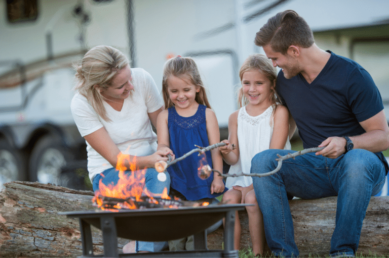 A family enjoying outdoor activities around a campfire with their RV in a scenic location.